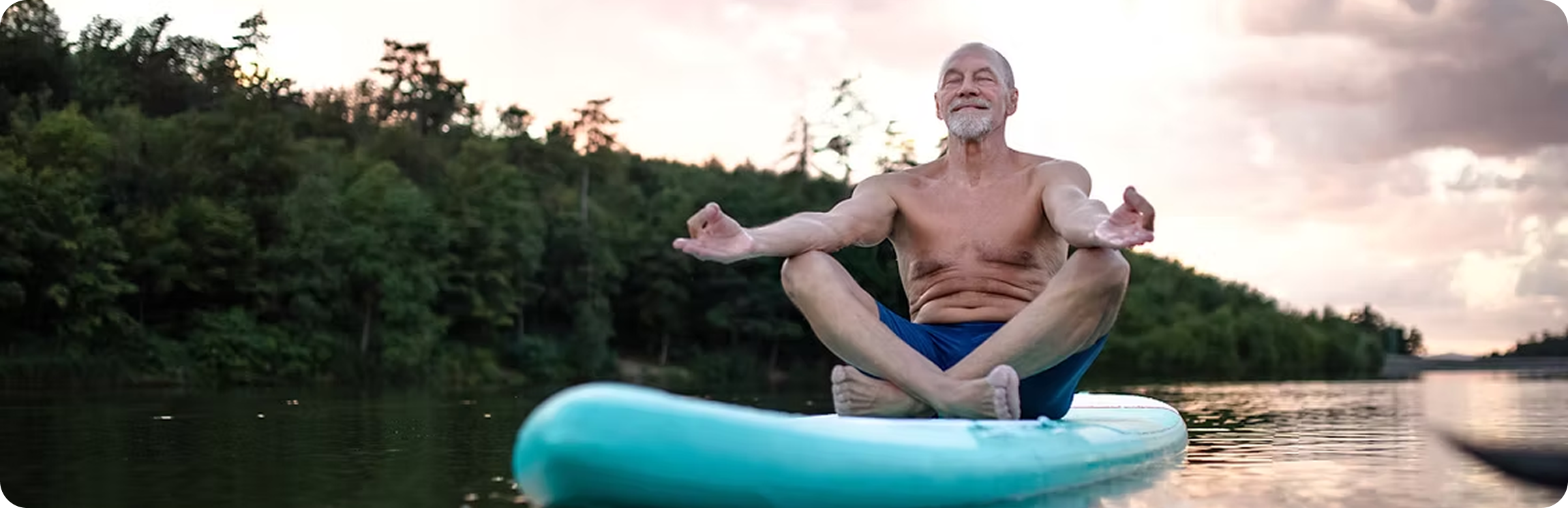 Man meditating on paddleboard in serene lake.